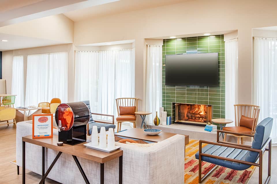 Modern living room with fireplace, green tile surround, wooden chairs, large windows, and contemporary furnishings