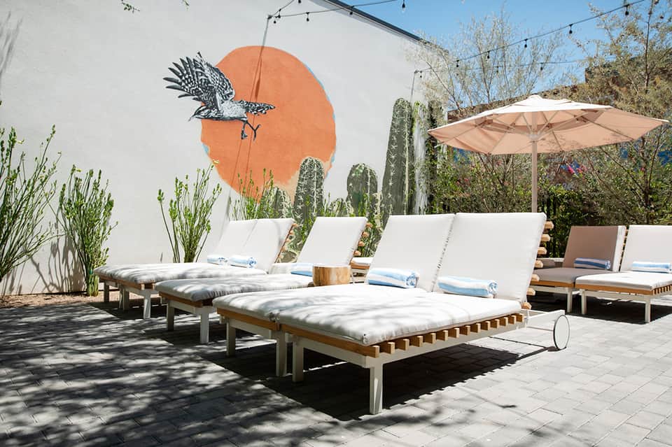 Contemporary poolside lounge with white cushioned chairs, orange mural, and desert landscaping