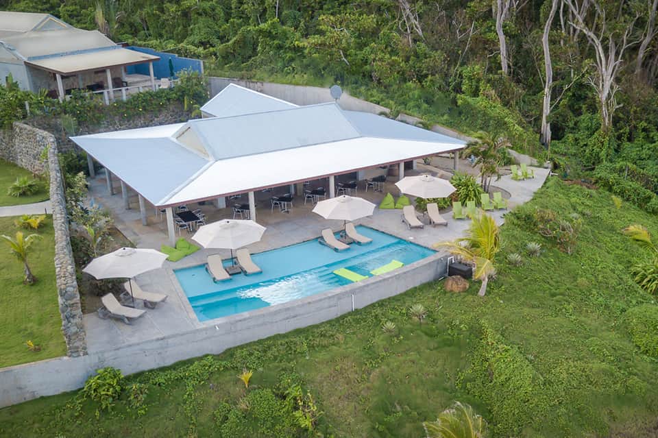 Aerial view of resort pool with white umbrellas and modern pavilion in jungle setting
