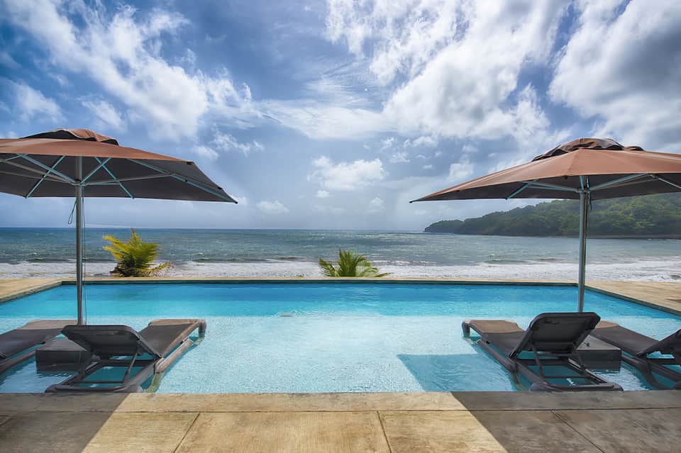Beachfront infinity pool with umbrellas overlooking ocean and tropical landscape