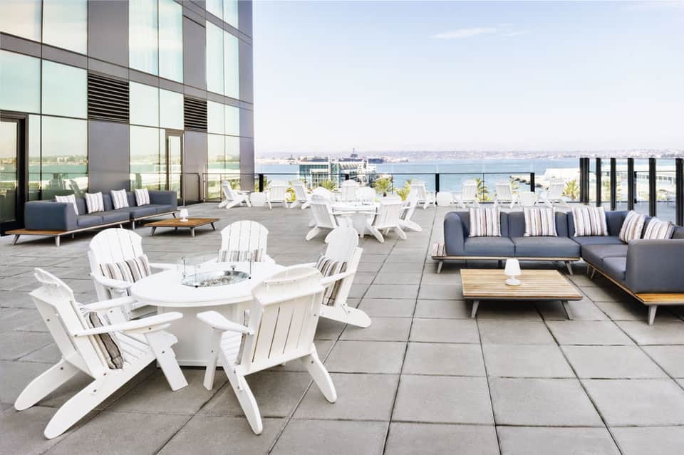 Rooftop terrace with white Adirondack chairs, modern seating areas, and waterfront city views