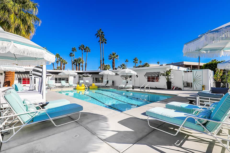 Modern resort pool with lap lanes, turquoise lounge chairs, white umbrellas, and palm trees
