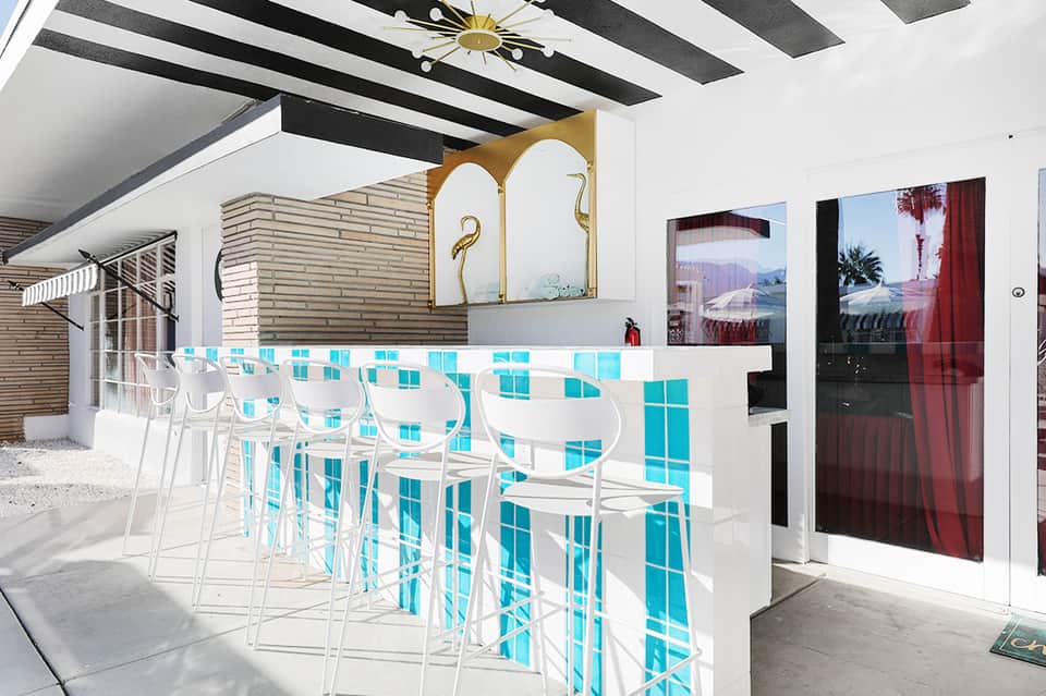 Modern hotel bar with turquoise tile accents, white chairs, contemporary ceiling design, and lounge area