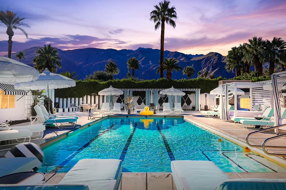 Luxury resort pool at dusk with striped cabanas, mountain views, and purple sunset sky