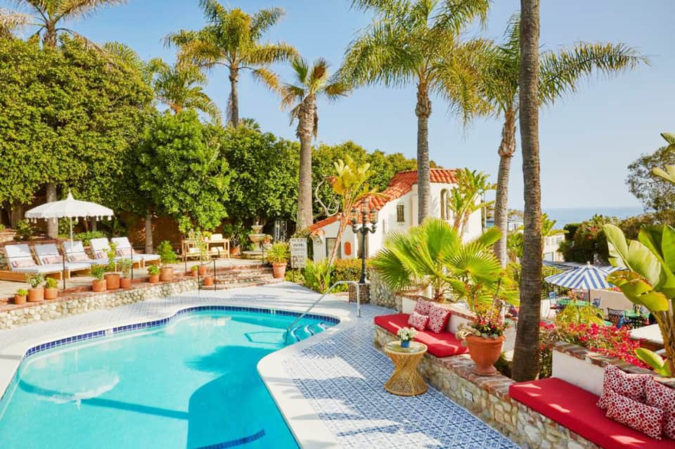 Resort pool with curved edges, palm trees, white Mediterranean-style building, and mountain views