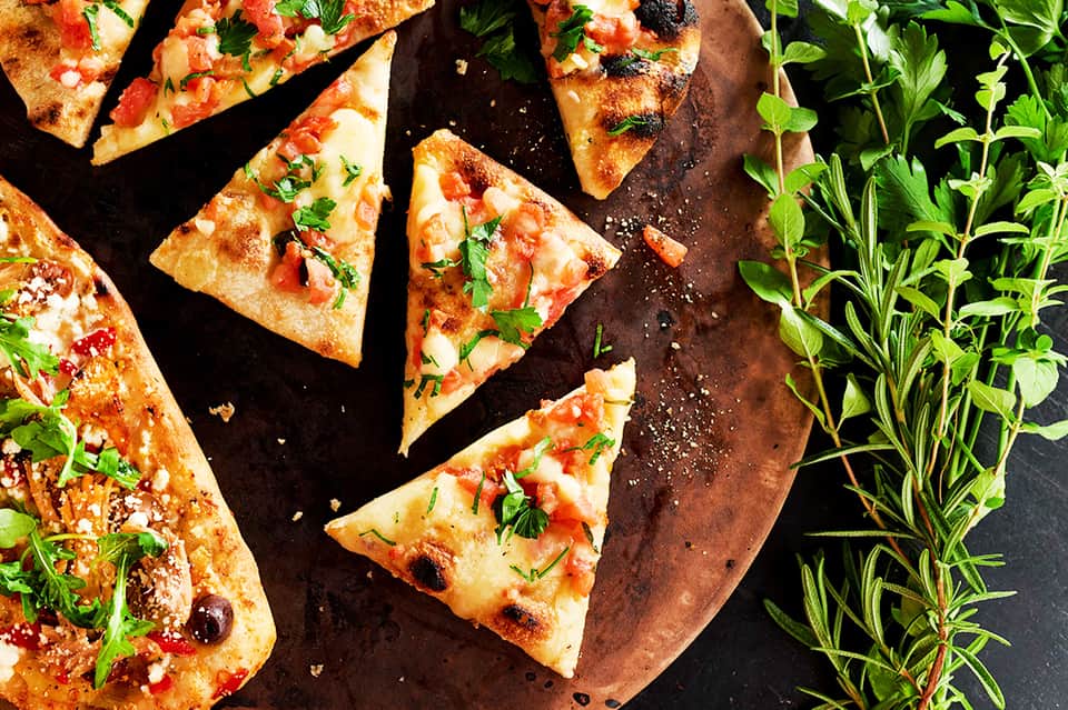 Fresh pizza slices garnished with basil on wooden serving board with herbs