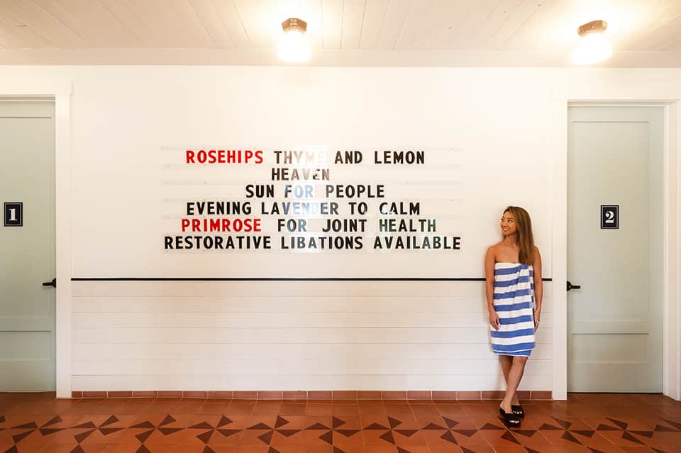Woman in striped dress beside wellness-themed text wall at spa entrance