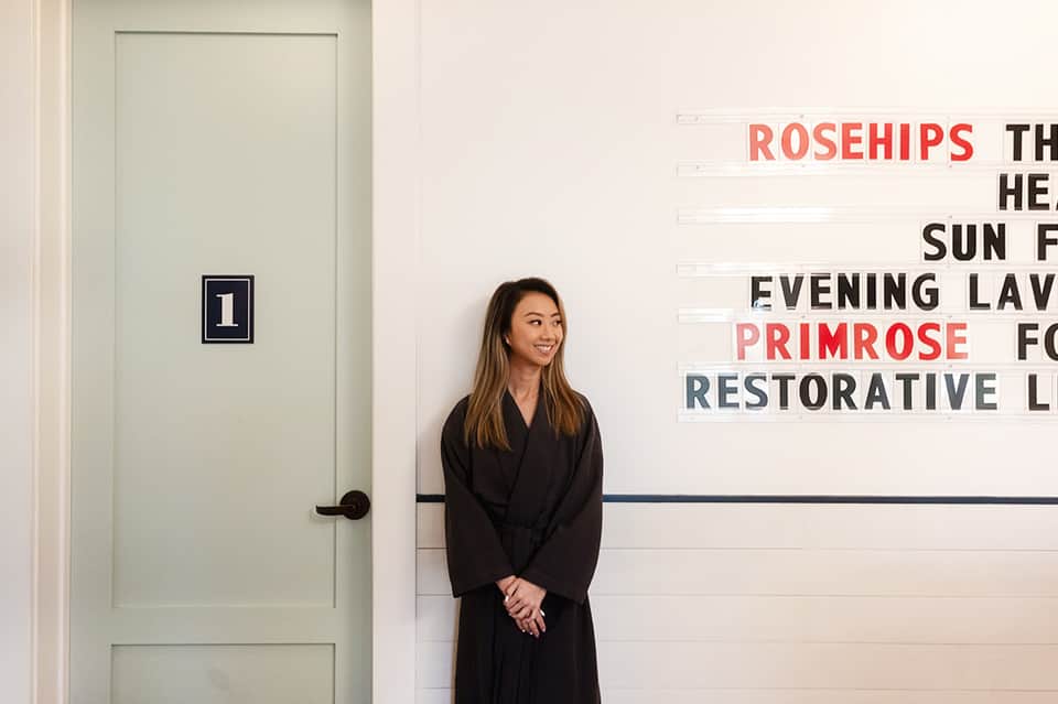 Woman standing in modern spa hallway with botanical wellness treatment signage