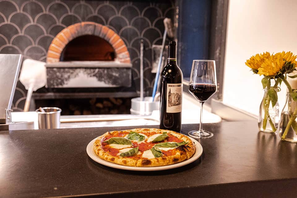 Gourmet pizza with wine and flowers beside wood-fired oven in upscale restaurant