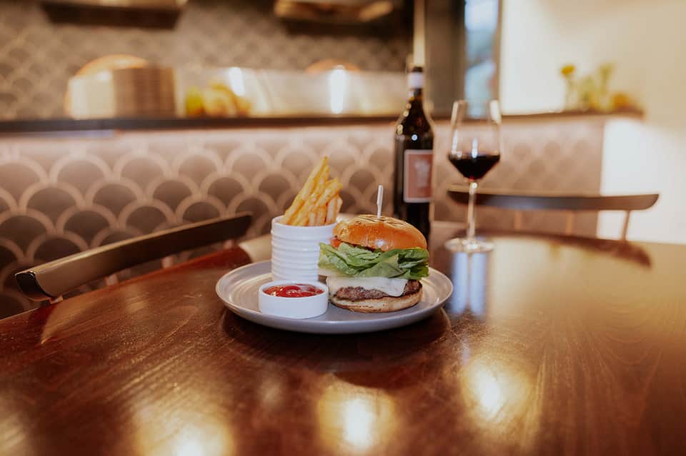 Gourmet burger and fries plated at restaurant counter with wine glass and patterned backsplash