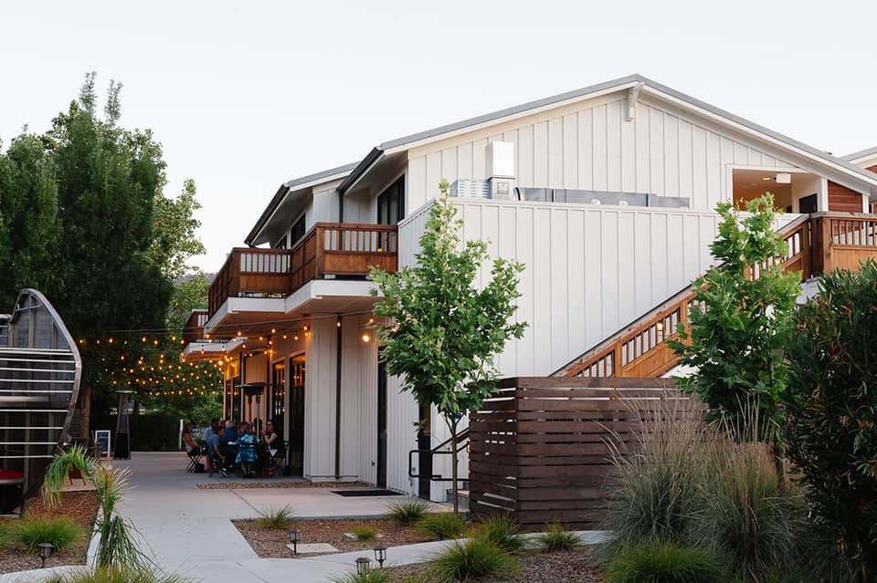 Modern residential building exterior with wooden decks, string lights, and contemporary design