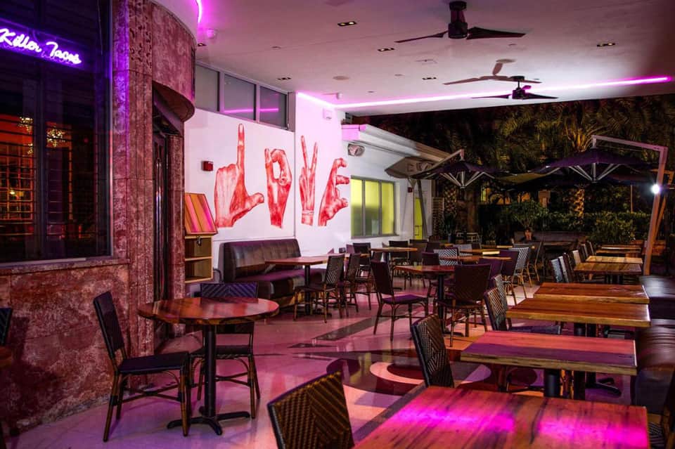 Modern nightclub interior with purple neon lighting, colorful art wall, and outdoor patio area