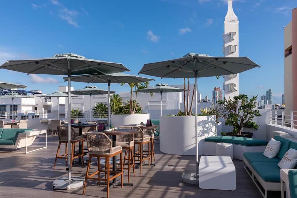 Rooftop terrace with gray umbrellas, high-top tables, modern furnishings, cityscape, and church steeple views.
