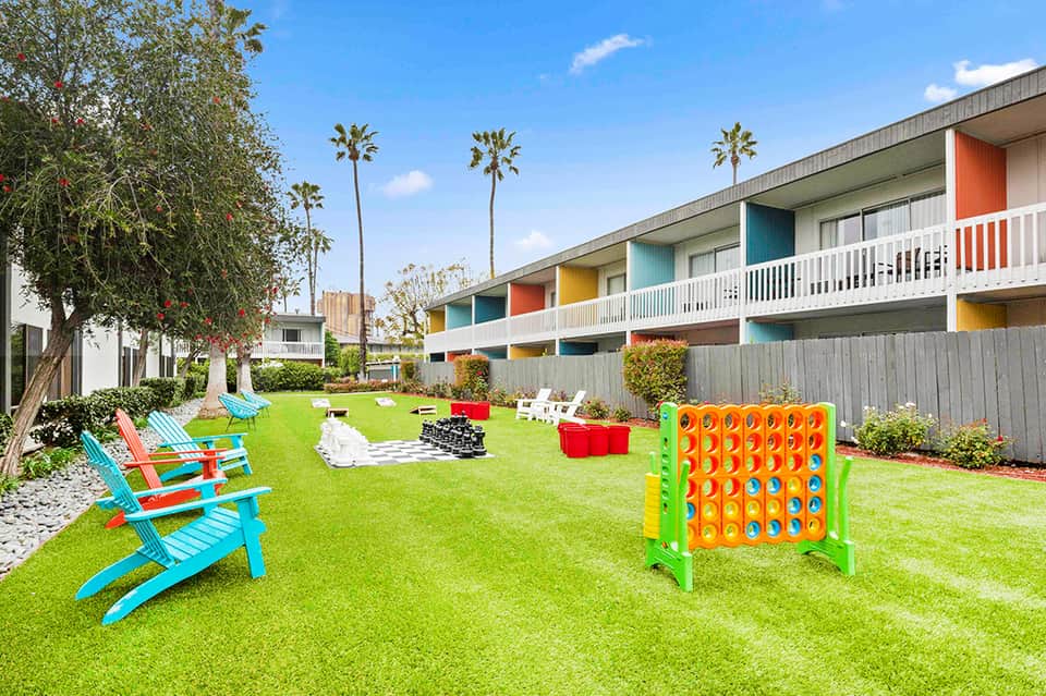 Family-friendly resort courtyard with colorful game board, adirondack chairs, and palm trees
