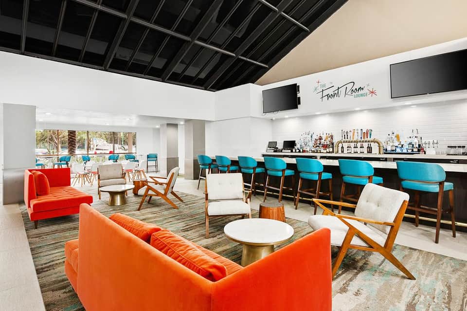 Modern resort lounge with vibrant orange and turquoise seating, bar area, and pool views