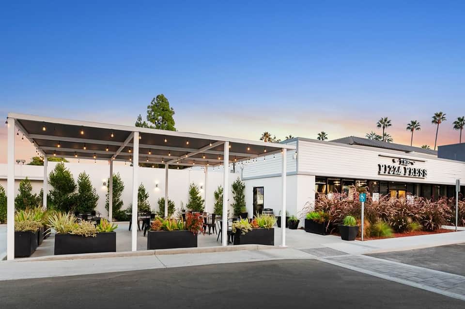 Modern white pergola-covered outdoor dining area with potted plants and contemporary restaurant storefront