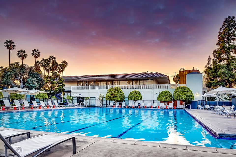 Olympic-sized swimming pool with lap lanes, loungers, and resort building at dusk