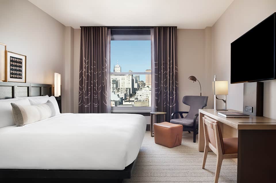 Modern hotel bedroom with white bedding, city skyline view, and contemporary furnishings