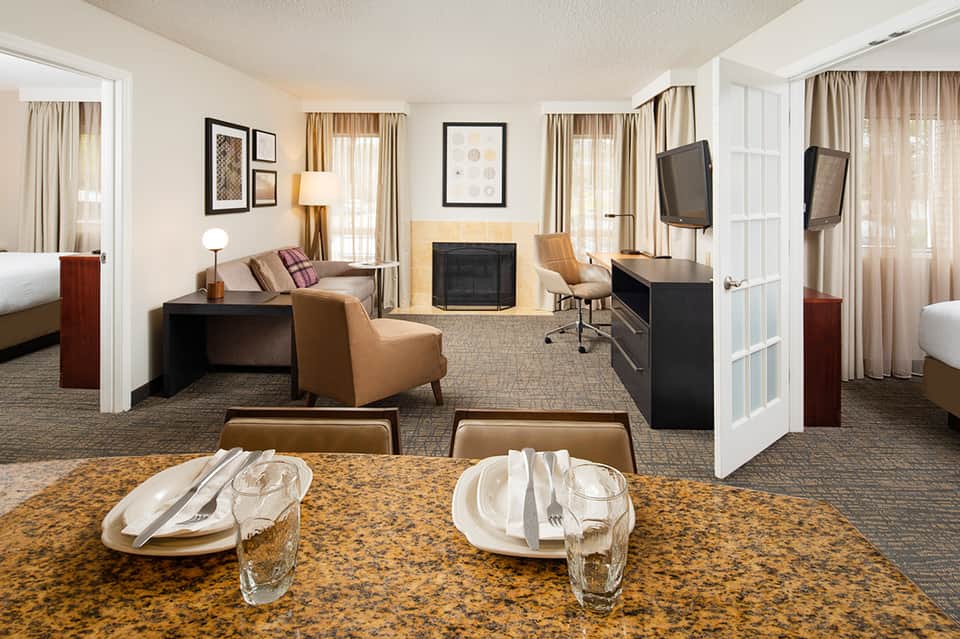 Upscale hotel suite with dining table, living area, fireplace, and separate bedroom