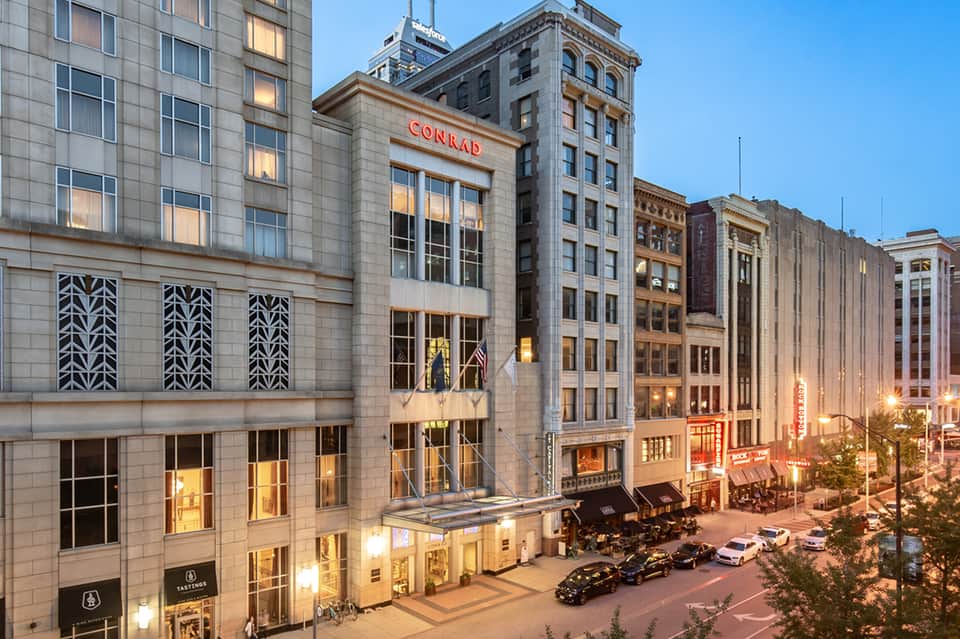 Urban hotel exterior showing Conrad hotel storefront on historic downtown street with evening lighting