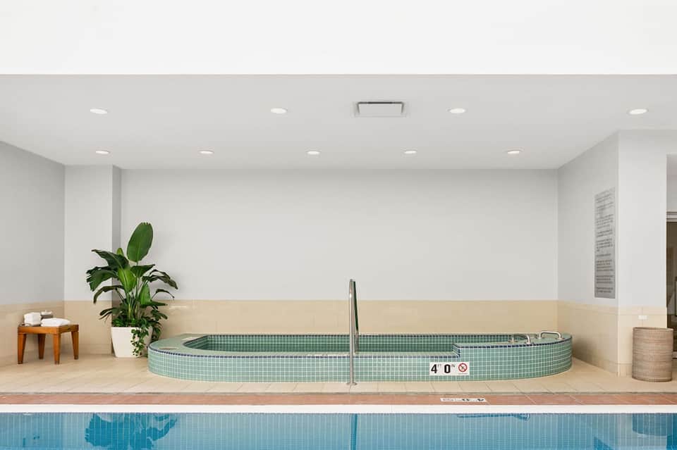 Spa soaking tub with green tile interior next to indoor lap pool with depth marker