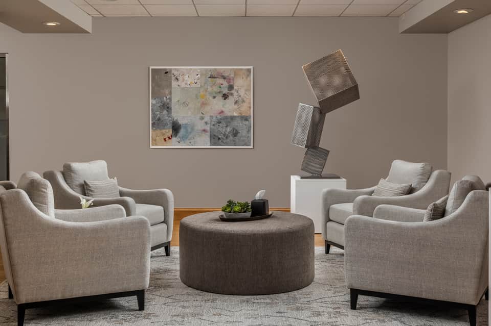 Modern lounge area with four cream upholstered chairs surrounding round ottoman, abstract art, and sculptural accent piece