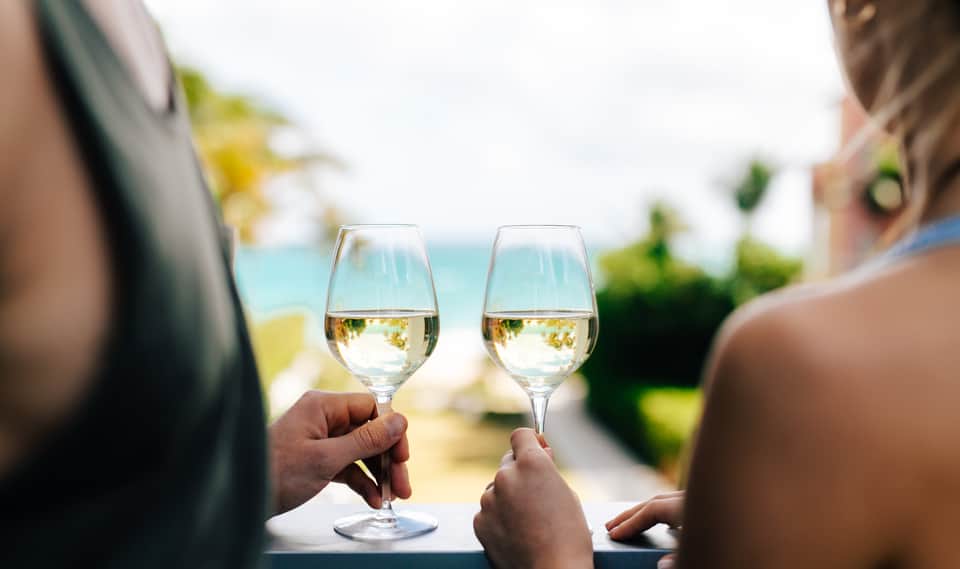 Two people toasting with white wine glasses overlooking a blue ocean coastline