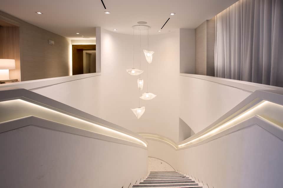 Modern hotel hallway with white walls, pendant lighting, mirrors, and contemporary architectural design