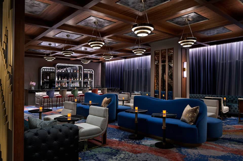 Elegant hotel lounge with wood coffered ceiling, blue velvet seating, and full bar with pendant lighting