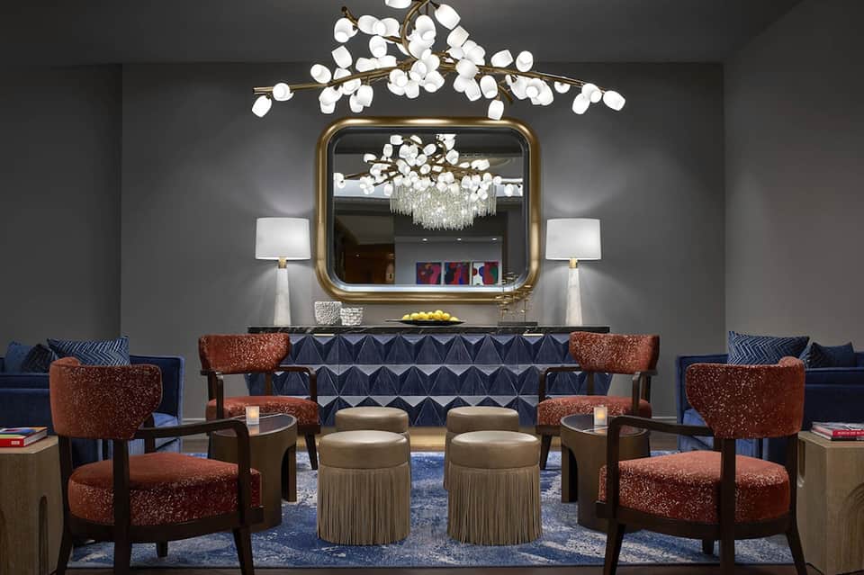Hotel lobby with gold-framed mirror, ornate chandelier, brown accent chairs, and patterned sofa