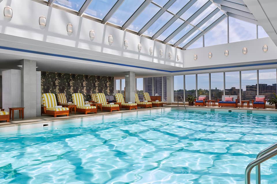 Rooftop indoor pool with skylights, yellow striped lounge chairs, city skyline views, and modern architecture