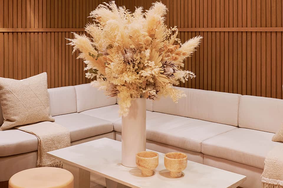 Minimalist lounge seating with cream cushions, pampas grass centerpiece, and corrugated wall