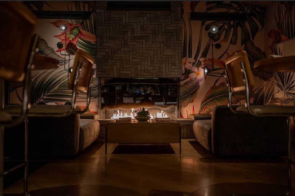 Modern lounge with fireplace, dark seating, tropical wall art, and ambient lighting