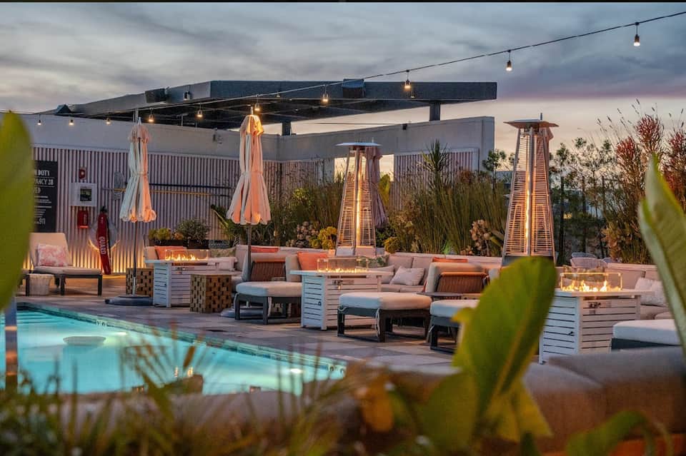 Rooftop pool at dusk with fire heaters, lounge seating, and desert landscape
