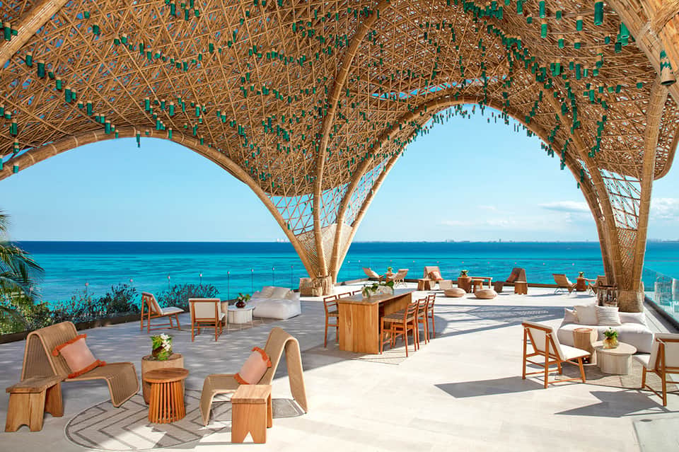 Upscale beach club with woven wooden architectural elements, ocean view, wooden furniture, and casual seating