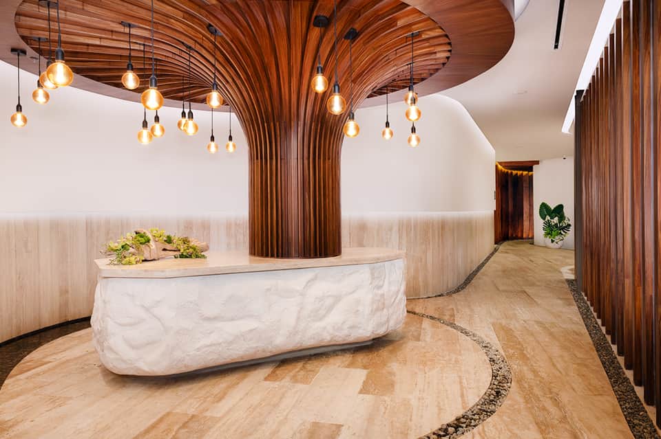Modern spa reception desk with curved wooden slat ceiling, marble counter, and pendant lights