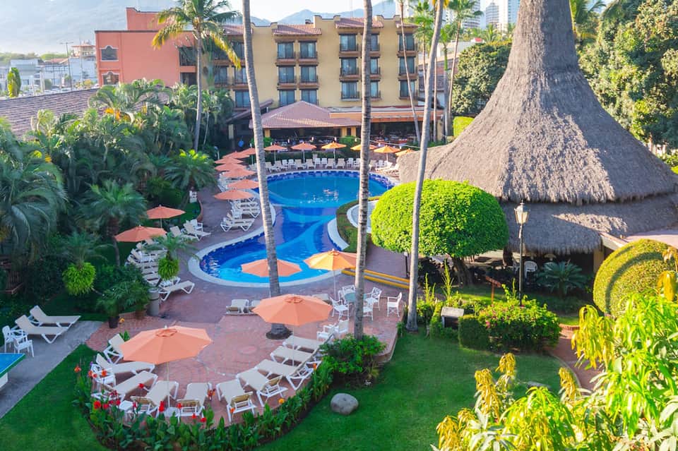 Resort pool with tiki bar, orange umbrellas, tropical landscaping, and hotel buildings