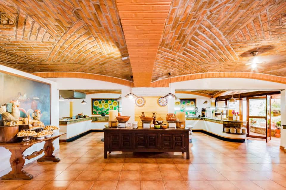 Spacious resort dining room with exposed wooden beam ceiling, buffet stations, and tropical artwork