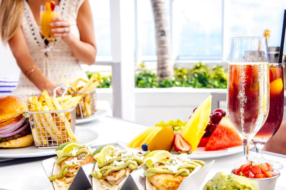 Tropical poolside dining with colorful cocktails, fresh fruit, and appetizers on white table