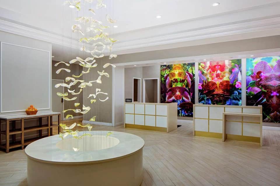 Modern resort lobby with sculptural pendant lighting, orchid artwork displays, and marble surfaces