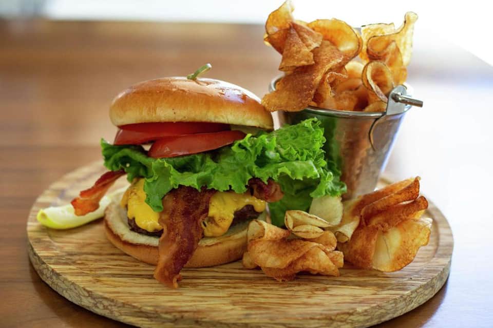Gourmet burger with bacon, lettuce, cheese, and crispy fries on wooden board