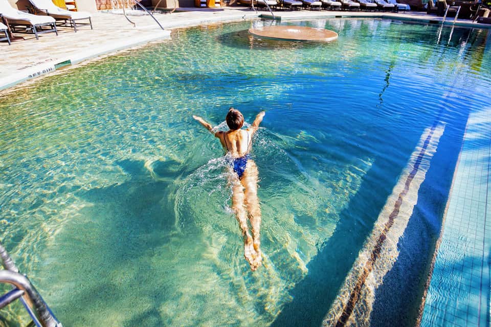 Young swimmer doing freestyle stroke in crystal-clear lap pool with lane dividers and lounge chairs