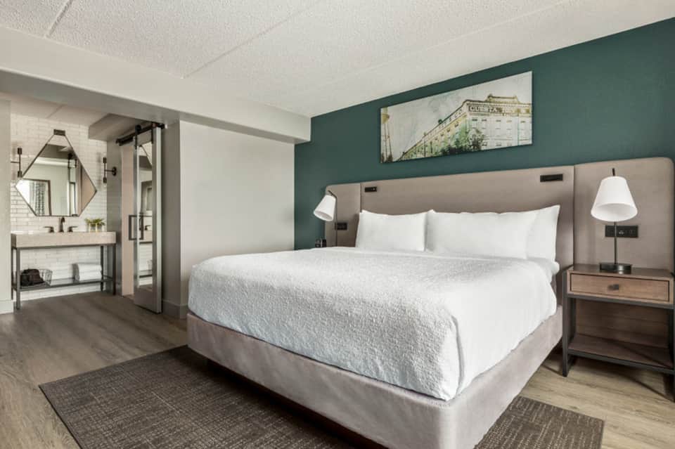 Modern hotel bedroom with queen bed, green accent wall, and en-suite bathroom