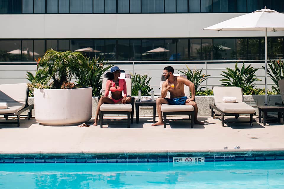 Contemporary pool deck with white lounge chairs, white umbrella, large planters, and modern building