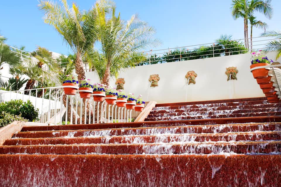 Resort courtyard with red brick steps, palm trees, and hanging flower planters