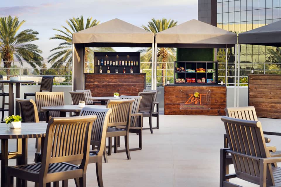 Rooftop lounge with tan umbrellas, wood service stations, and palm tree surroundings
