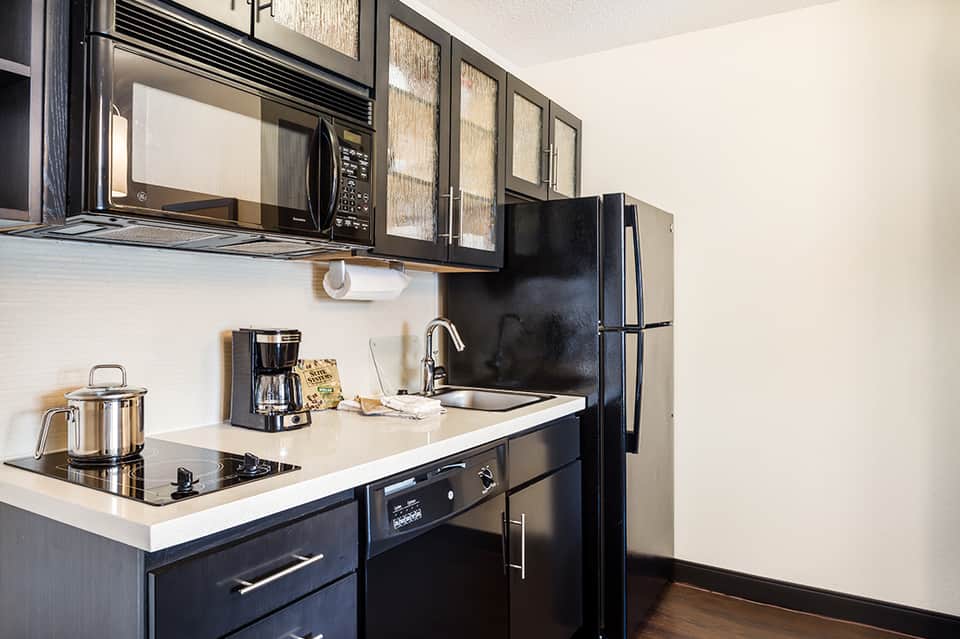 Modern hotel kitchenette with black cabinets, white countertop, and stainless steel appliances