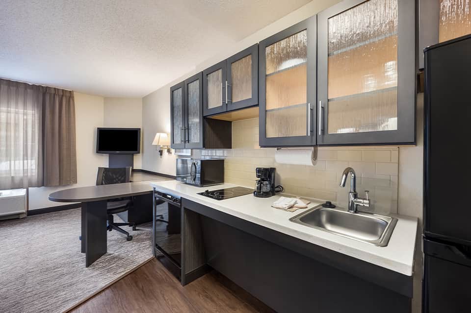 Hotel suite kitchenette with black cabinetry, desk area, and TV