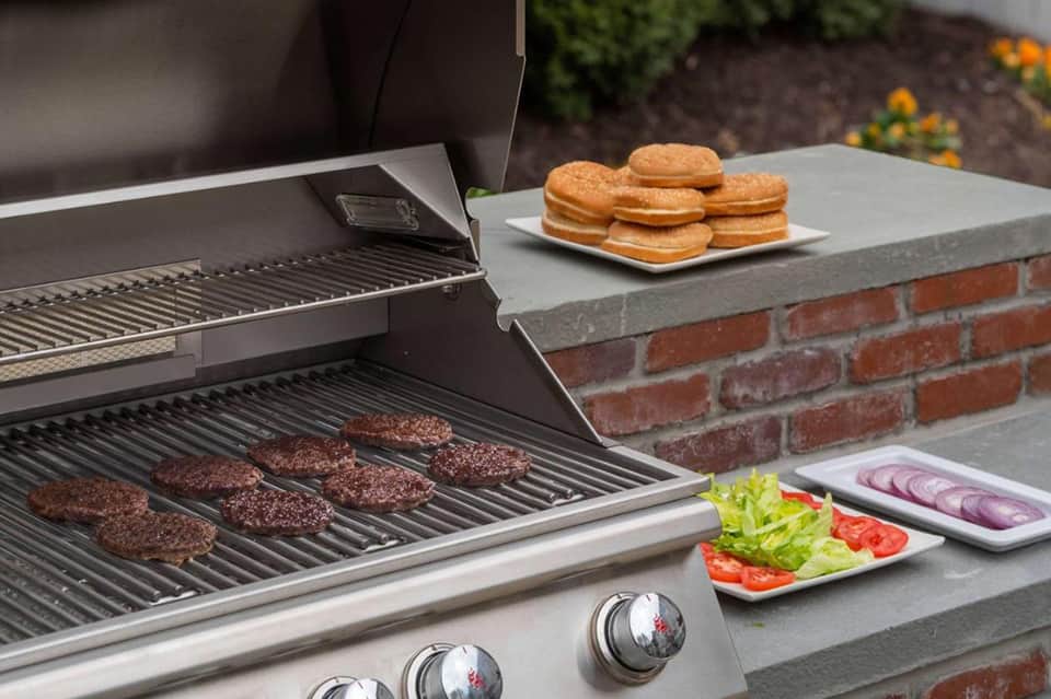 Outdoor grill cooking hamburgers with donuts and fresh vegetables on adjacent counter