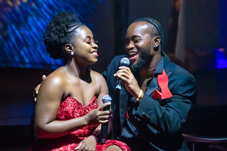 Couple performing duet with microphones on stage with blue lighting and professional backdrop